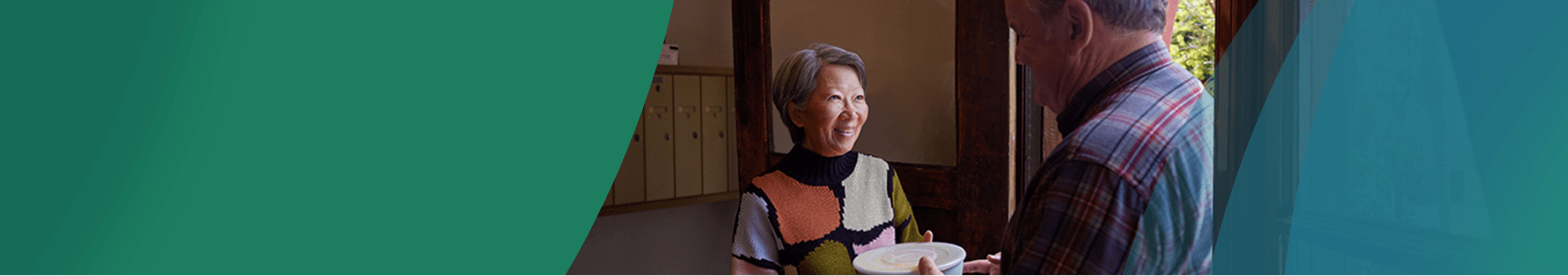 An Asian woman in her 60s with short gray hair meets her neighbor, a White man in his 60s, in the lobby of her apartment building. The man is handing her a container full of soup and they are smiling at each other. Actor portrayals.