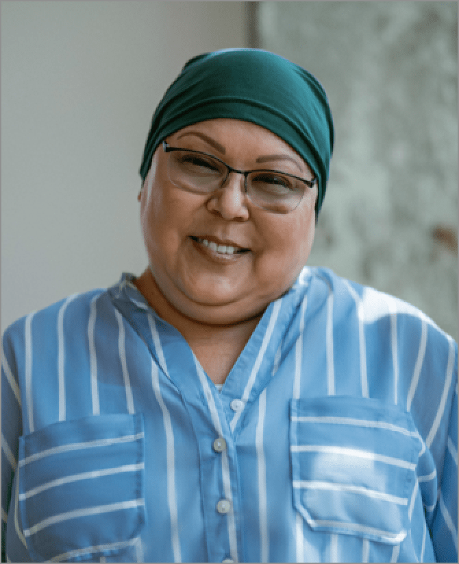 Lisa, a woman receiving TRODELVY, sits smiling at the camera. Lisa is a Latina woman wearing a headscarf, glasses, and a blue shirt with white stripes.