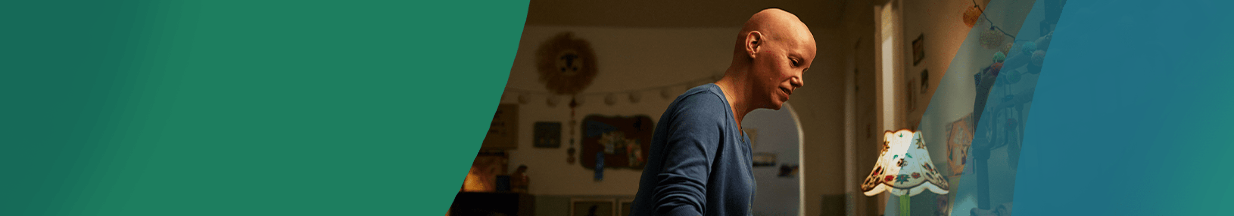 A White woman in her 40s with no hair is sitting on the side of her young daughter's bed, tucking her in for the night. They are softly smiling at each other. Actor portrayals.