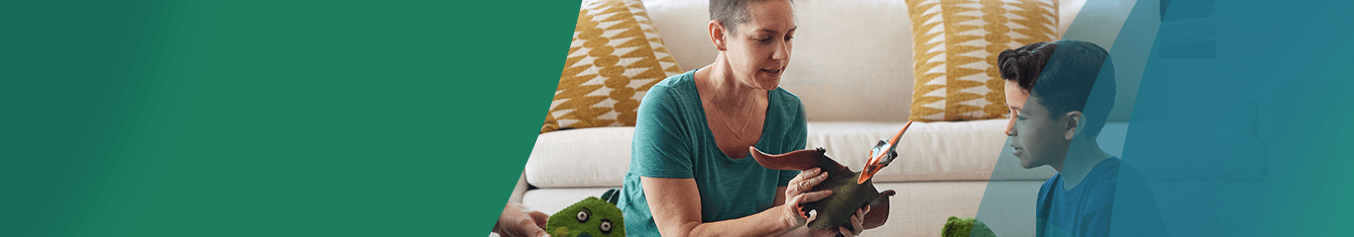 A White woman in her 30s with shaved dark hair sits on the living room floor in front of the couch between a White man in his 30s and a 7-year-old boy. The woman is holding a dinosaur action figure and is playing with the boy, who has a dinosaur puppet on his hand. Actor portrayals.