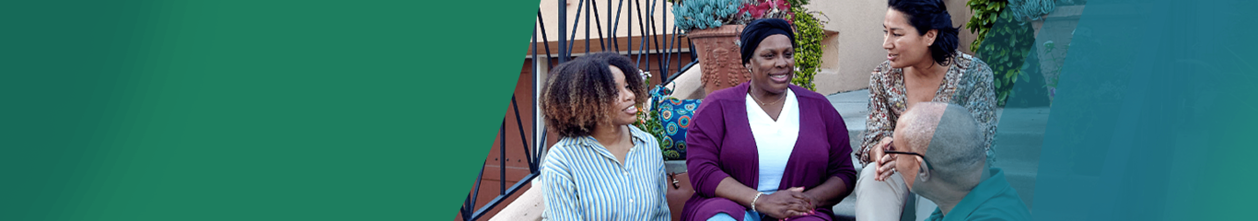 A Black woman in her 40s wearing a Black hair wrap is sitting outside on the stairs of her front porch with 3 of her friends and neighbors. They are all smiling and talking. Actor portrayals.