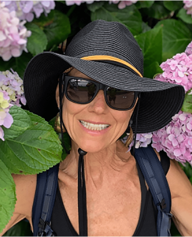 Karen, a woman receiving TRODELVY, is smiling at the camera. Karen is a White woman wearing a black sun hat and sunglasses.