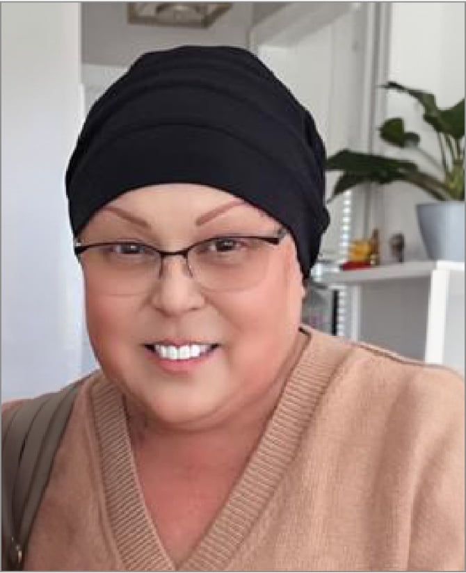 Lisa, a woman receiving TRODELVY, sits smiling at the camera. Lisa is a Latina woman wearing a headscarf, glasses, and a tan shirt.