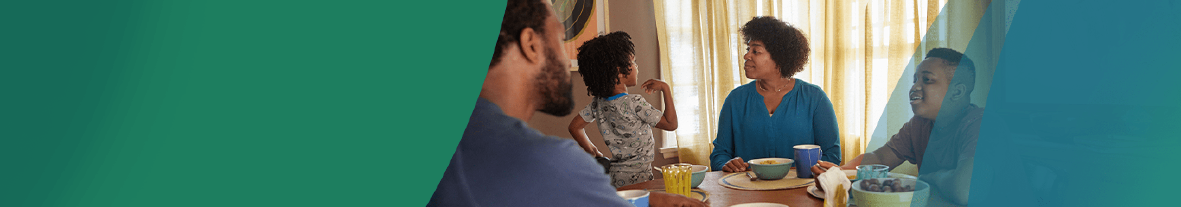 A father, a mother, and their two children sit around a table. Actor portrayals.