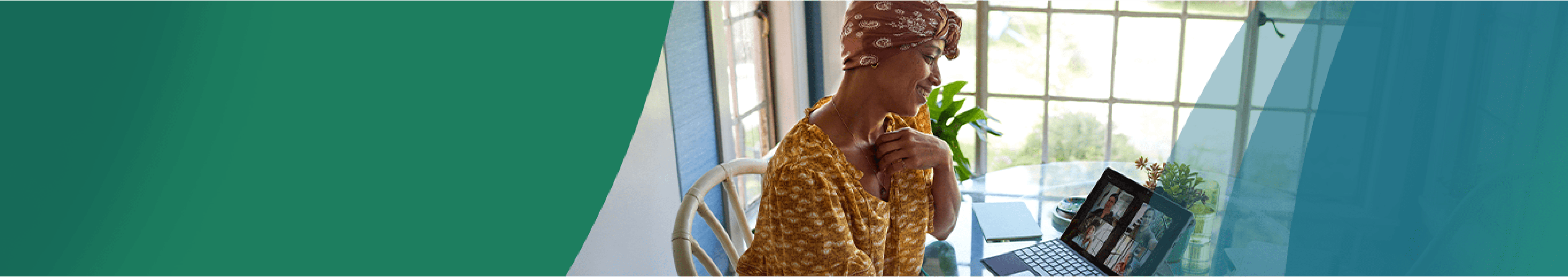 A Black woman in her early 40s wearing a paisley headscarf and a patterned yellow shirt sits in a brightly lit room at a round glass table smiling at her tablet screen, on a video call with her close group of friends. A potted plant, notebook, and notepad sit on the table with her. Actor portrayals.