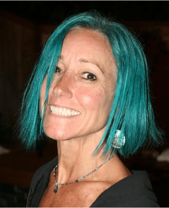 Karen, a woman receiving TRODELVY, is standing outside smiling at the camera. Karen is a White woman wearing a blue wig, and a black shirt.