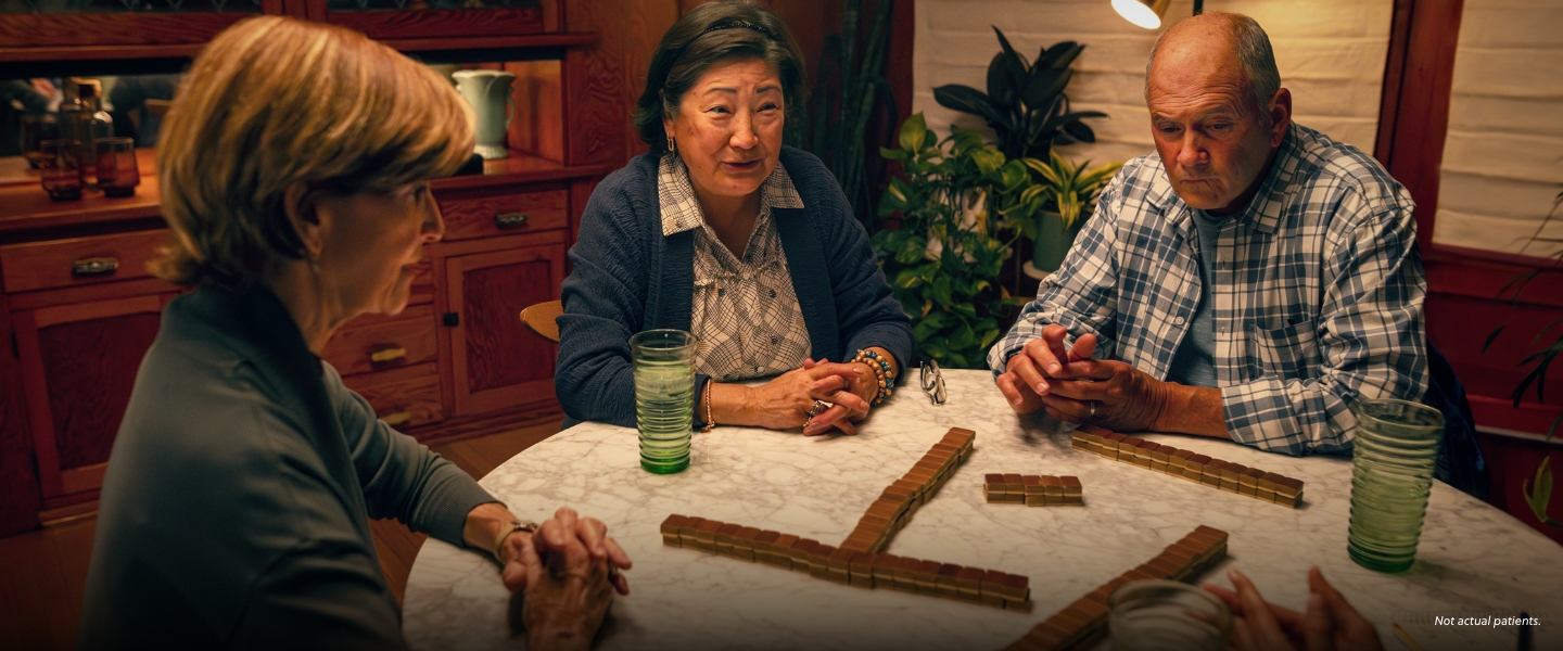 A white man, a white woman, and an asian woman in their 60s are sitting at a dining room table, playing a board game. Not actual patients.