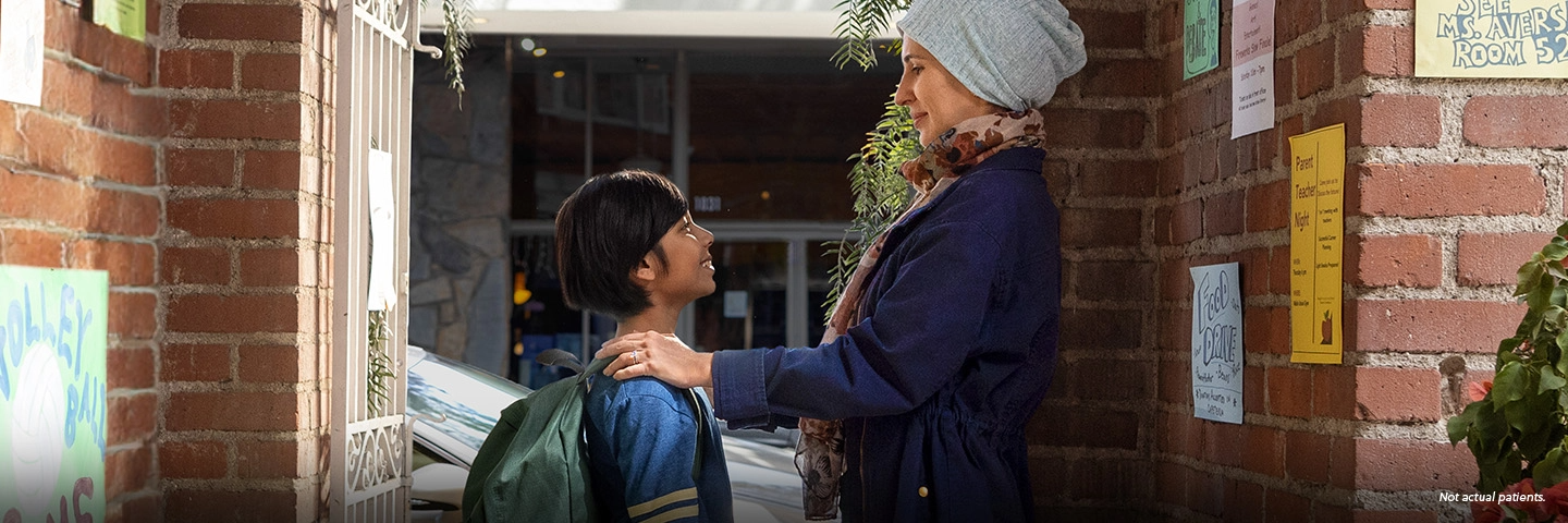 A Latina woman in her 40s wearing a light blue knit hat is dropping her 10-year-old son off at school. They are standing in the doorway facing each other, and the woman has her hands on the boy's shoulders. Not actual patients.