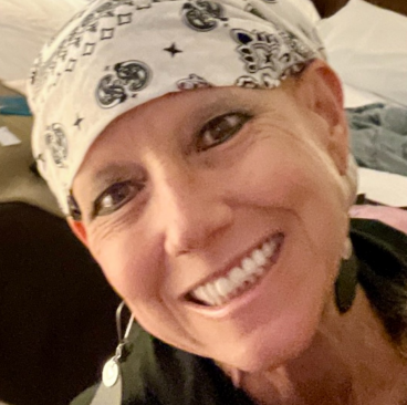 Karen, a woman receiving TRODELVY, is smiling at the camera. Karen is a White woman wearing a white bandana, and a green shirt.
