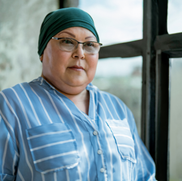 Lisa, a woman receiving TRODELVY. Lisa is a Latina woman wearing a headscarf, glasses, and a blue shirt with white stripes.